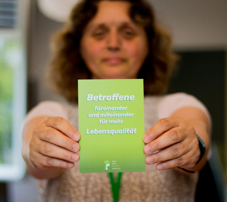 Frau zeigt Postkarte: Betroffene füreinander und miteinander für mehr Lebensqualität